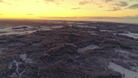 Panorama-view-of-icy-wooden-winter-landscape-during-golden-sunset-at-sky---aerial-wide-shot