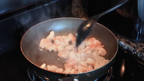Stirring-a-frying-pan-of-chicken,-cooking-on-the-stove
