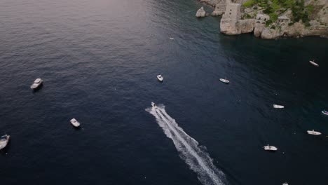 Speedboat-In-Turquoise-Ocean-Near-Cliffside-Village-Of-Positano-In-Amalfi-Coast,-Campania,-Italy