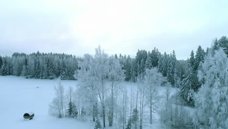 Aerial-dolly-shot-of-barrel-sauna-covered-with-snow,-Scenic-white-forest,-Winter-season