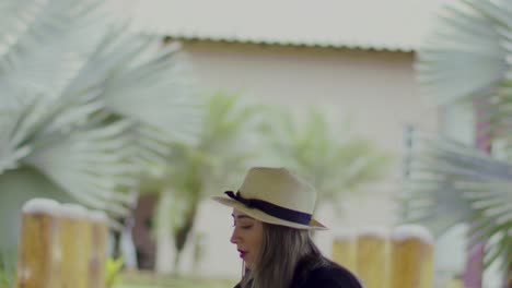 lady-in-a-straw-hat-puts-a-glass-and-bottle-of-red-wine-on-a-table-in-the-garden-with-palm-trees---close-up-slow-motion