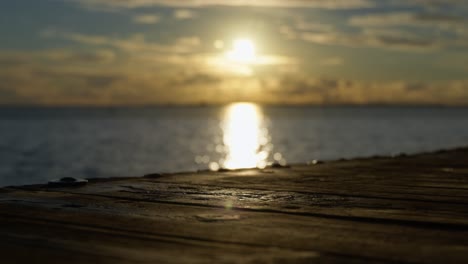 Focus-shifts-from-a-wooden-pier-to-sun-setting-over-the-North-Sea-in-Germany,-sunset-over-sea
