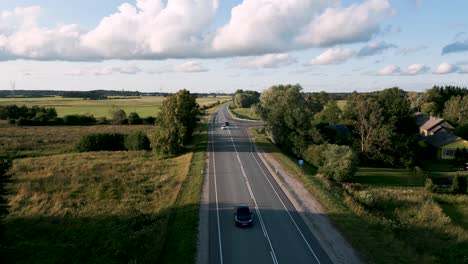 Estonia---Aerial-drone-flightover-country-road-with-overtaking-cars---flyover-following-a-romantic-street-with-upcoming-cars-in-a-travel-atmosphere-with-cloudy-blue-sky