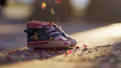 Colorful-Confetti-Falling-on-Baby-Shoes-Backlit-with-Warm-Light-In-slow-motion