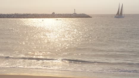 Goldene-Stunde-Am-Venedig-Strand-Von-Los-Angeles,-Segelboot-Und-Kajak-Segeln-Am-Ozean,-Die-Wellen-Und-Der-Sand-Werden-Vom-Sonnenuntergang-Golden-Beleuchtet,-Zeitlupe