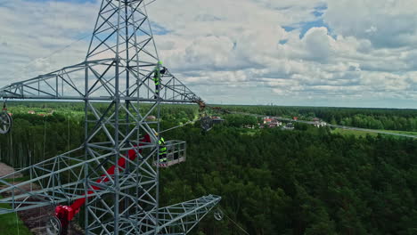 Aerial-view-of-two-worker-repairing-or-installing-transmission-tower-in-forest-during-cloudy-day---close-up