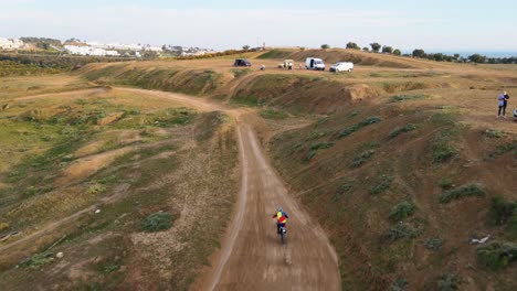 Aerial-dolly-tracking-shot-of-a-motorcyclist-on-a-dusty-motocross-track-in-Malaga-in-Spain-with-dusty-path-and-people-watching-the-stunts-of-the-motocross-rider-on-the-hills