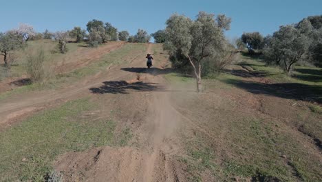Aerial-tracking-dolly-shot-of-a-driving-motocross-on-a-motocross-track-in-Malaga-Spain-with-dusty-track,-trees-and-hills-on-a-cloudless-sunny-day
