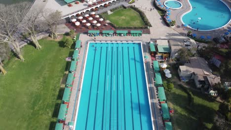 Drone-video-of-an-olympic-sized-swimming-pool-surrounded-by-green-grass-and-trees