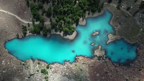 Cinematic-drone-shot-of-turquoise-colored-water-in-the-mountains-at-Naltar-Valley-in-Pakistan,-downward-angle-aerial-shot