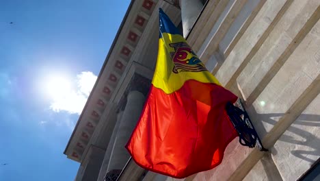 Moldovan-flag-on-facade-flagpole-against-bright-sunlight,-low-angle