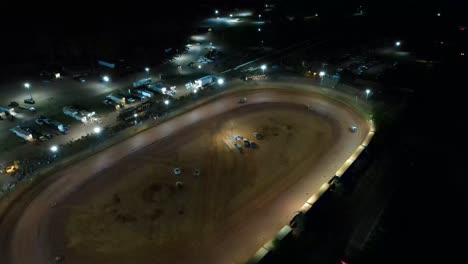 Aerial-orbit-of-race-car-racing-on-oval-dirt-track-at-night