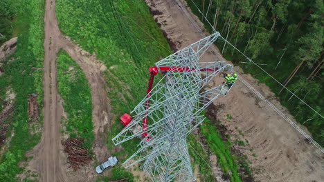Top-shot-of-workers-installating-power-line-pylon-with-the-help-of-tall-red-crane-at-daytime