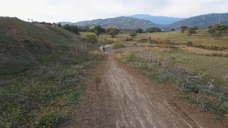 Dolly-Luftaufnahme-Einer-Ländlichen-Motocross-Strecke-In-Malaga,-Spanien-Mit-Hügeln,-Gras-Und-Bergen-Im-Hintergrund-Mit-Einem-Motocross-Fahrrad,-Das-über-Einen-Hügel-Springt