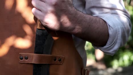 Man-puts-large-knife-into-a-leather-strap-on-an-apron