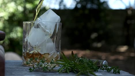 Whiskey-is-poured-into-a-high-ball-class-with-ice-in-an-outdoor-setting-under-some-trees