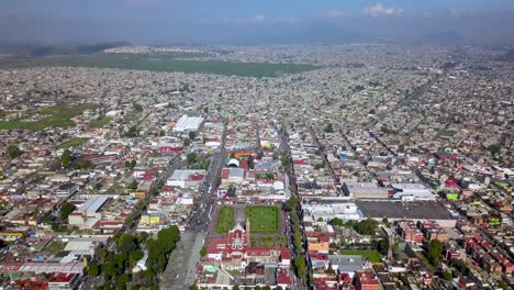 Top-drone-view-of-a-catholic-church-in-the-charming-town-of-chalco-Mexico,-and-view-of-the-downtown-and-roads-towards-Mexico-City
