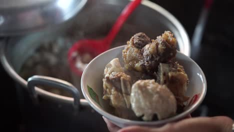 Hands-take-meatballs-from-pot-to-bowl-containing-beef-bones