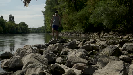Man-stepping-across-rocks-next-to-a-river-on-a-nature-hike-in-slow-motion