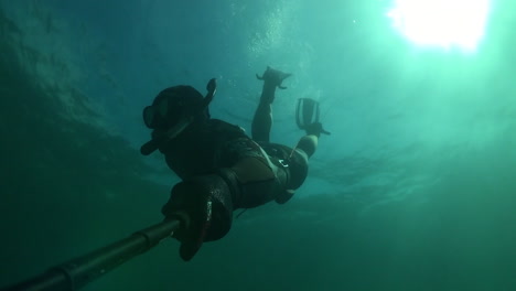Man-duck-dives-underwater-wearing-full-wetsuit-in-cold-water-and-holding-a-selfie-stick-with-go-pro