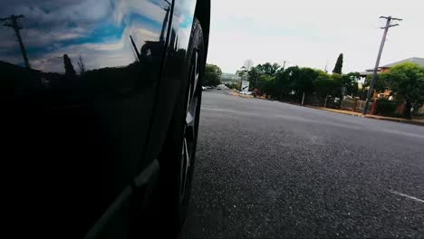 Car-POV-from-road-facing-front-right-wheel-driving-down-bitumen-road-down-a-hill-into-town