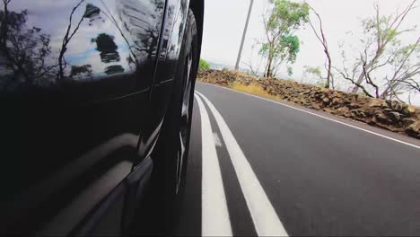 Car-POV-from-road-facing-front-right-wheel-driving-down-bitumen-road-down-a-hill-into-town