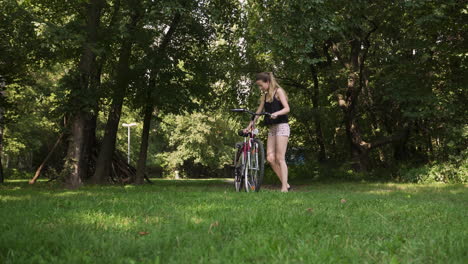 Una-Mujer-Bonita-Aparca-Su-Bicicleta-En-Un-Parque-Cubierto-De-Hierba