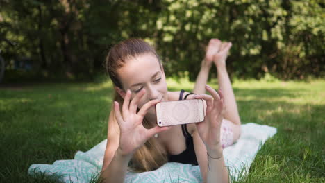 Beautiful-caucasian-woman-laying-in-a-grassy-field-taking-a-picture-with-her-smart-phone