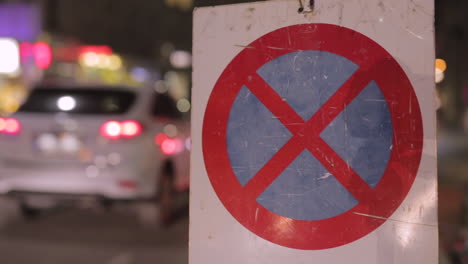 No-parking-sign-in-the-night-with-passing-traffic-in-the-background