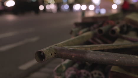 Blurred-out-night-time-traffic-in-the-background-with-a-stack-of-pipes-and-fence-pieces-in-the-foreground