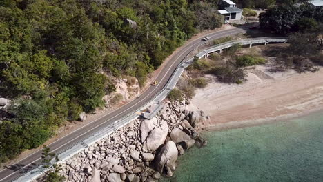 Aerial-view-of-open-top-convertible-classic-beach-buggy-driving-along-rocky-coastal-clifftop-road-next-to-crystal-clear-tropical-water