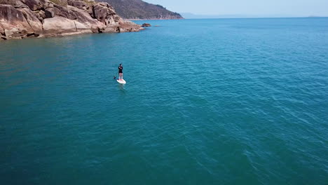 Luftaufnahmen-Von-Drohnen,-Die-Um-Ein-Einsames-Weibliches-Paddleboarding-In-Richtung-Einer-Luxusyacht-An-Einem-Abgelegenen-Inselziel-Kreisen