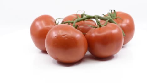 Five-red-tomatoes-held-together-with-vine-spinning-around-on-white-platform