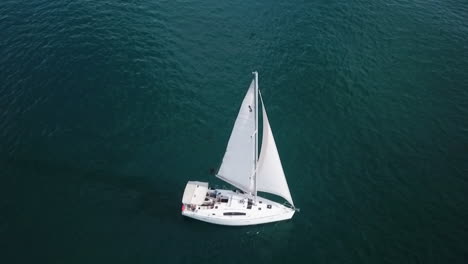Top-view-aerial-footage-of-white-yacht-sailing-slowly-in-calm-blue-seas
