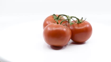 Three-red-tomatoes-on-truss-spinning-around-on-white-surface