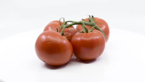 Four-red-ripe-tomatoes-spinning-on-white-platform