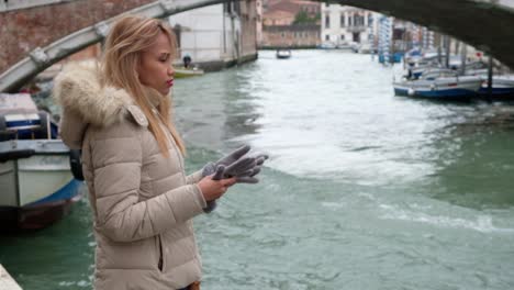 Philippina-is-standing-beside-a-canal-in-Venice-and-puts-on-gloves-to-protect-herself-from-the-cold-weather-as-she-is-watching-canal-boats-pass-by
