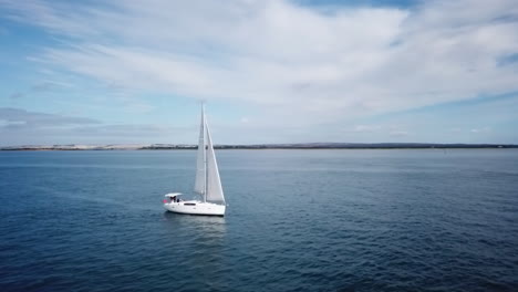 Aerial-footage-panning-around-luxury-yacht-sailing-slowly-in-deep-blue-water-near-shore
