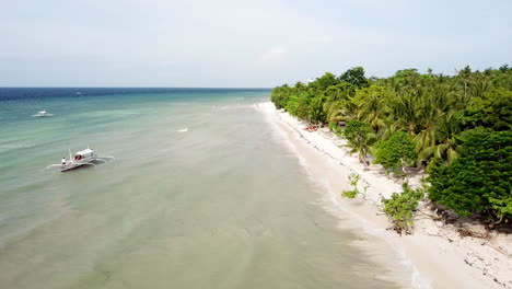 AERIAL-footage-tracking-along-beautiful-white-sandy-beach-with-palm-trees-and-turquoise-water-with-traditional-fishing-boats-on-Panglao-Island-in-the-Phillipines