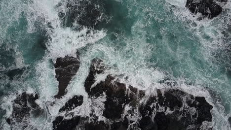 Aerial:-Turbulent-ocean-waves-crashing-over-dark-basalt-rock-ledges