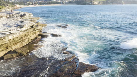 Während-Gesäumte-Wellen-Auf-Ozeanfelsen-Krachen,-Bewegt-Sich-Die-POV-Drohne-Langsam-Von-Der-Klippenwand-Weg-Coogee-Beach-Sydney-Australien