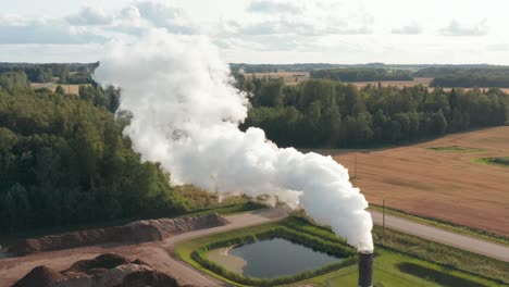 Aerial-drone-shot-of-a-lone-factory-chimney-spewing-fumes-into-atmosphere-in-rural-area