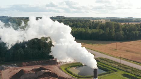 Aerial-drone-shot-of-a-lone-factory-chimney-spewing-fumes-into-atmosphere-in-rural-area