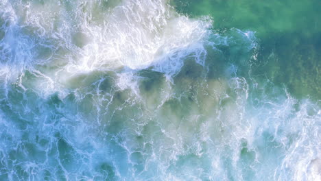 White-fringed-waves-rolling-in-from-top-of-screen-onto-shallow-sandy-coastline-Tamarama-beach-Sydney-Australia-POV-drone