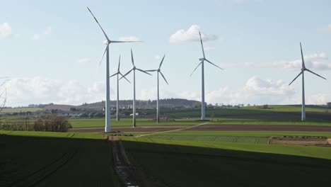 Windkraftanlagen-Drehen-Sich-Auf-Einem-Feld-Mit-Weg-Zum-Dorf-Im-Hintergrund