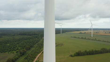 Upward-aerial-close-up-of-a-rotating-wind-turbine-with-wind-turbine-park-in-the-background