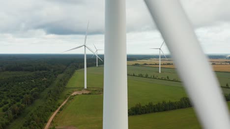 Upward-aerial-close-up-of-a-rotating-wind-turbine-with-wind-turbine-park-in-the-background