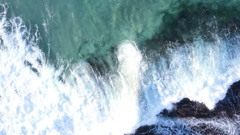 Weiße-Gesäumte-Wellen,-Die-Vom-Oberen-Rand-Des-Bildschirms-Auf-Ozeanfelsen-Rollen,-Tamarama-Beach,-Sydney,-Australien,-POV-Drohne,-Die-Nach-Links-Verfolgt