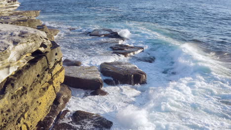 Large-waves-crashing-onto-ocean-rocks-POV-drone-moving-forward-along-cliff-face-Coogee-Beach-Sydney-Australia
