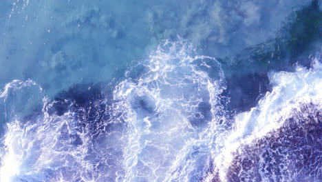 White-fringed-waves-crashing-in-from-top-of-screen-onto-ocean-rocks-Tamarama-Beach-Sydney-Australia-POV-drone-directly-above-and-pan-right-then-pull-away